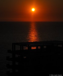 Solen i ferd med å gå ned bak et hotellet som er i ferd med å bli bygget ved sjøkanten.