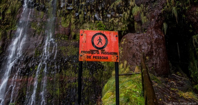 Til høyre er inngangen hvor  en låst dør stenger muligheten til å gå videre. Øverst på venstre side av skiltet er et lite svart området hvor man kunne gå bak fossen før.